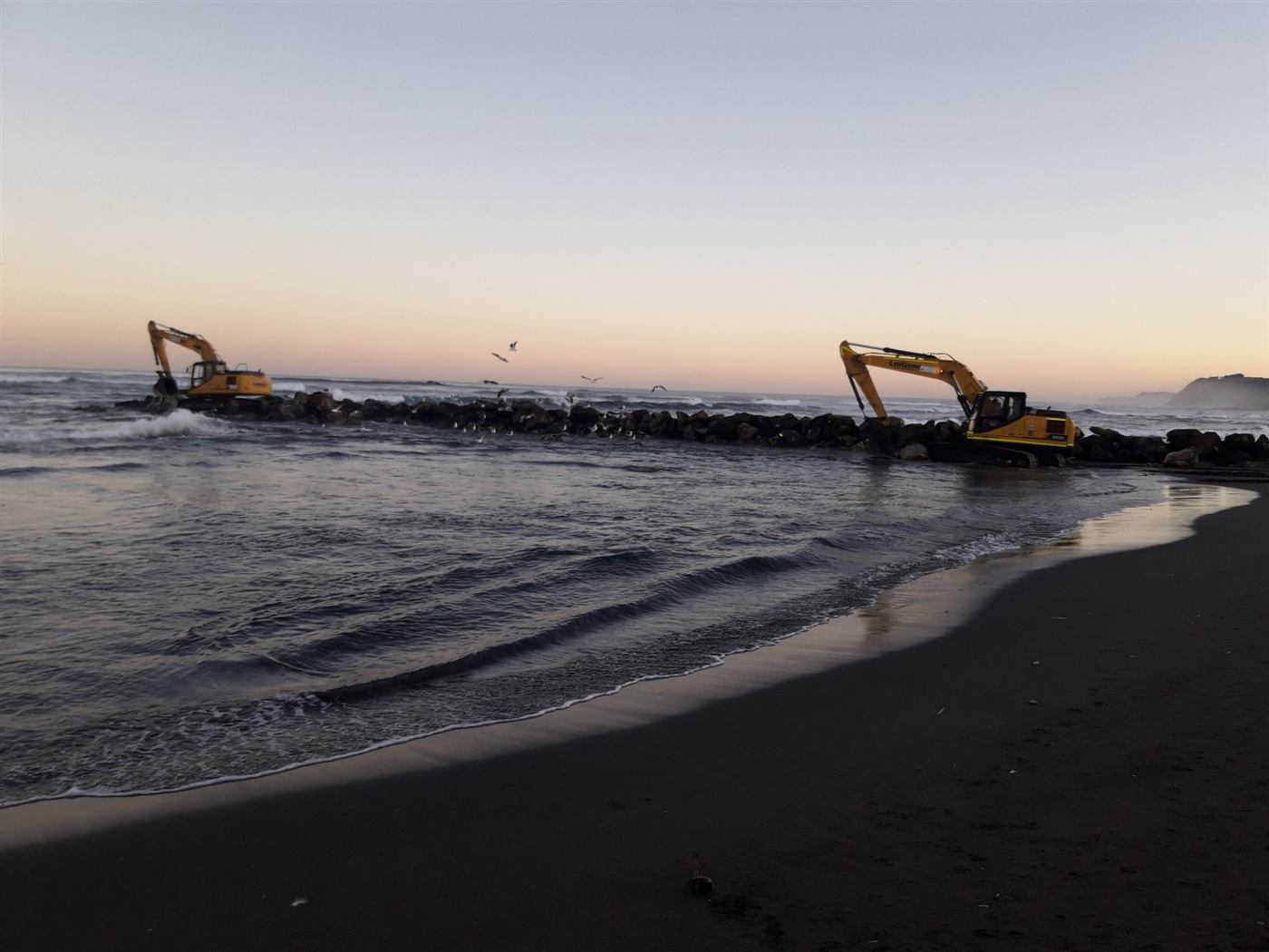 Maquinaria trabajando en obra marítima al atardecer